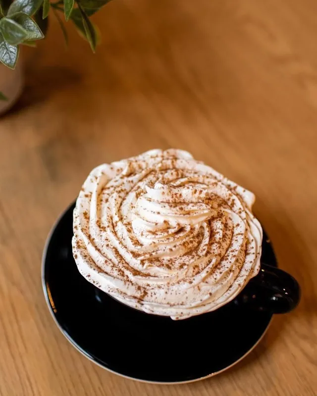 Un cappuccino con crema batida y canela servido en taza negra en O Positivo