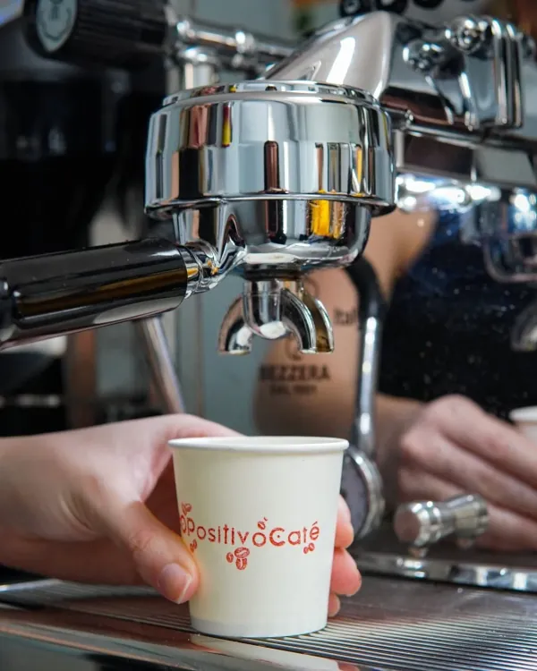 Un barista de O Positivo saca un espresso en la máquina, con un vaso de O Positivo Café en la mano
