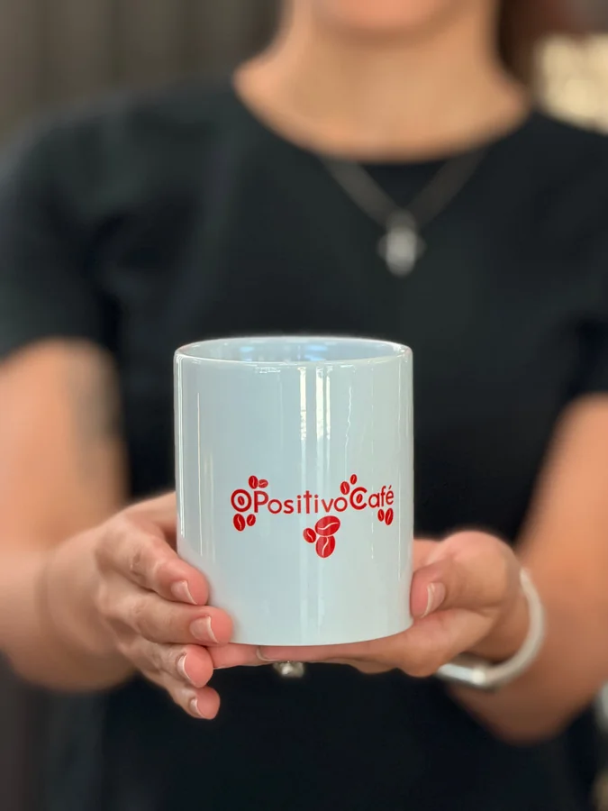 Manos sosteniendo una taza blanca con el logo rojo de O Positivo Café